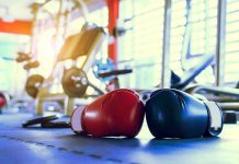 Boxing gloves on gym floor with equipment.