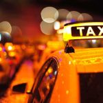 Close-up of a taxi sign illuminated at night with blurred city lights in the background
