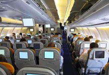 Interior view of an airplane with passengers seated and using in-flight entertainment screens