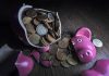 A broken pink piggy bank with coins spilling out onto a wooden surface