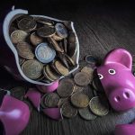 A broken pink piggy bank with coins spilling out onto a wooden surface