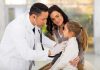 A doctor examines a young girl with a stethoscope while her mother watches