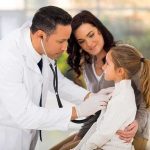 A doctor examines a young girl with a stethoscope while her mother watches