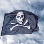 A black pirate flag featuring a skull and crossbones waving against a cloudy sky