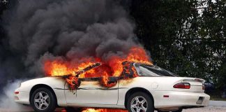 A white car engulfed in flames with thick black smoke rising