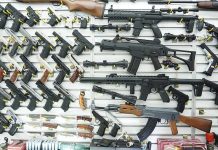 Gun Store Owners Slammed With New Regulations Wall display of various firearms in a store.