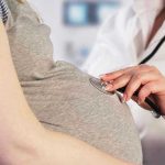 Doctor uses stethoscope on pregnant womans belly.