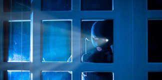 Criminal STRIKES While Family Mourns Champion Masked figure peering through glass door at night.