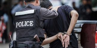 Police officer arrests handcuffed person.