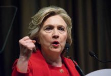 Person speaking passionately at a podium, wearing red jacket.