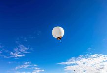 A white balloon floating in a clear blue sky with scattered clouds