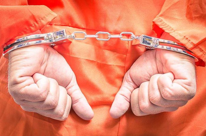 shutterstock_163027793.jpg Hands in handcuffs wearing an orange jumpsuit