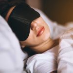Woman sleeping with a black sleep mask in a cozy bed