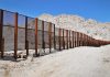 A long border wall stretches across a desert landscape with mountains in the background