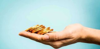 A hand holding a stack of gold coins against a light blue background