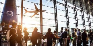 Crowd of travelers in airport terminal with airplane outside.