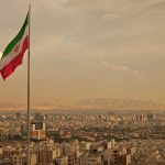 Iran Faces Total Destruction? Trump’s Final Warning Looms Iranian flag waving over a city skyline with mountains in the background