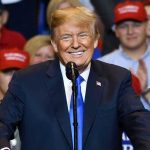 Holiday Split: Trump Honors Fallen, Slams Foes Man in suit speaking at rally with red hats.