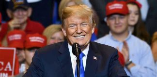 Holiday Split: Trump Honors Fallen, Slams Foes Man in suit speaking at rally with red hats.