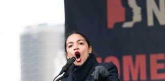 AOC’s STINGING Accusation: ‘Proven Bigot’ Exposed! Woman speaking passionately at podium during outdoor event.