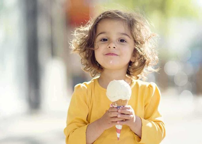 A young child with curly hair holding an ice cream cone outdoors