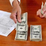 California’s Unprecedented 100% Tax Standoff Sparks Legal Chaos Hands counting cash and reviewing financial documents on a wooden table