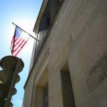 Mass Purge Looms Inside Washington American flag at Department of Justice building exterior.