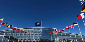 NATO Shakeup Looms — Europe’s Free Ride Ends Flags outside NATO headquarters building under clear blue sky.