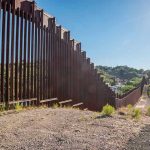 Cartel Super Tunnel Under U.S. Port Tall metal border wall with rural landscape.