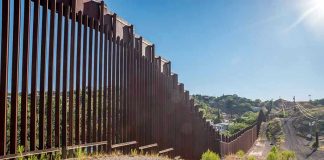 Cartel Super Tunnel Under U.S. Port Tall metal border wall with rural landscape.