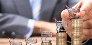 Mini shopping carts on stacks of coins, business background.