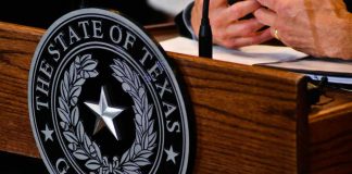 ICE Grabs Voter Data — What’s Inside? Close-up of the Texas governors seal on a wooden podium with hands gesturing in the background