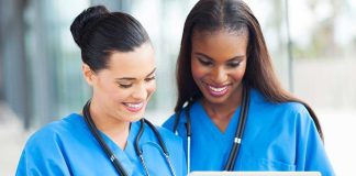 Fake Nurses Everywhere? Two nurses in blue scrubs smiling while looking at a tablet