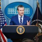Hegseth Unleashes Leak War Man speaking at podium with flags in background