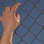Hand gripping a chain-link fence