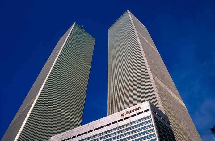 Twin rectangular skyscrapers rising above a hotel facade against a clear blue sky