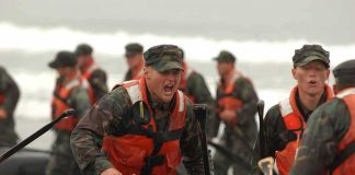 Soldiers in life vests haul an inflatable boat from the surf