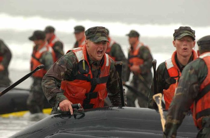 Soldiers in life vests haul an inflatable boat from the surf