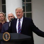 man speaking at podium with officials standing behind