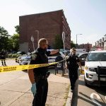 Police officers secure an urban street with yellow tape near patrol cars