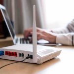 Wi‑Fi router on desk with person typing on laptop