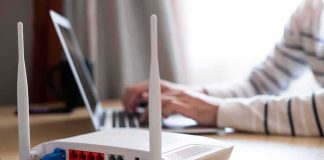 Wall-Penetrating 6G Sparks Privacy Fight Wi‑Fi router on desk with person typing on laptop