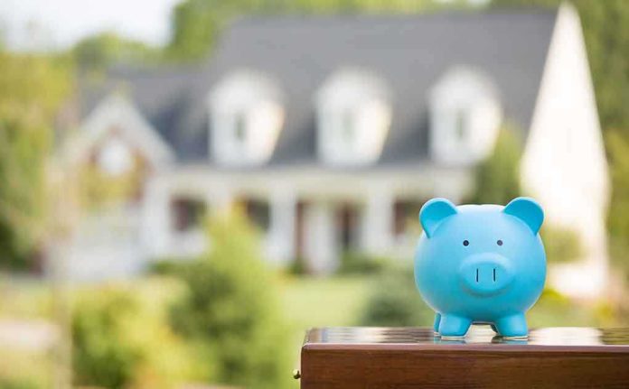 shutterstock_219244759 A blue piggy bank in front of a blurred house and greenery