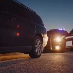 Police officer stands by patrol car during traffic stop at dusk