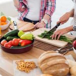 Hands chopping fresh herbs on a cutting board beside assorted produce