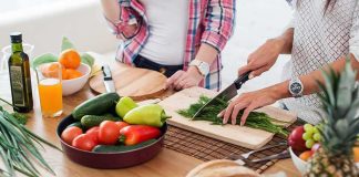 Hands chopping fresh herbs on a cutting board beside assorted produce
