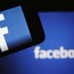 Facebook logo on a smartphone with blurred Facebook screen behind