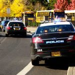 Police cars with lights on near school buses on a city street
