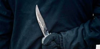 Blood-Licking Text Explodes In Karmelo Anthony Case Gloved hand holding a serrated knife against a dark jacket