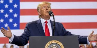 Nuclear Gamble: Trump Teases Kim Showdown speaker at podium with U.S. flag backdrop